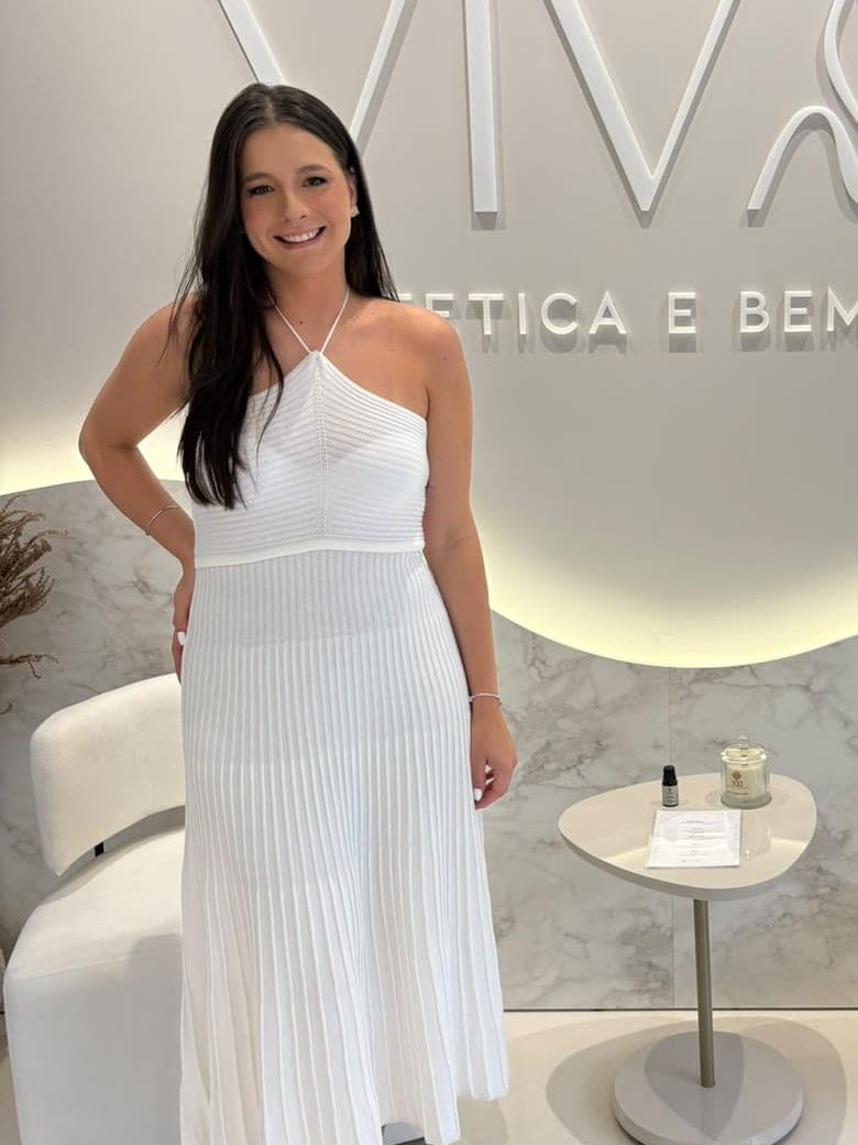 Dra. Carolina Vaz sorrindo, de vestido branco, na recepção da Vivaz
